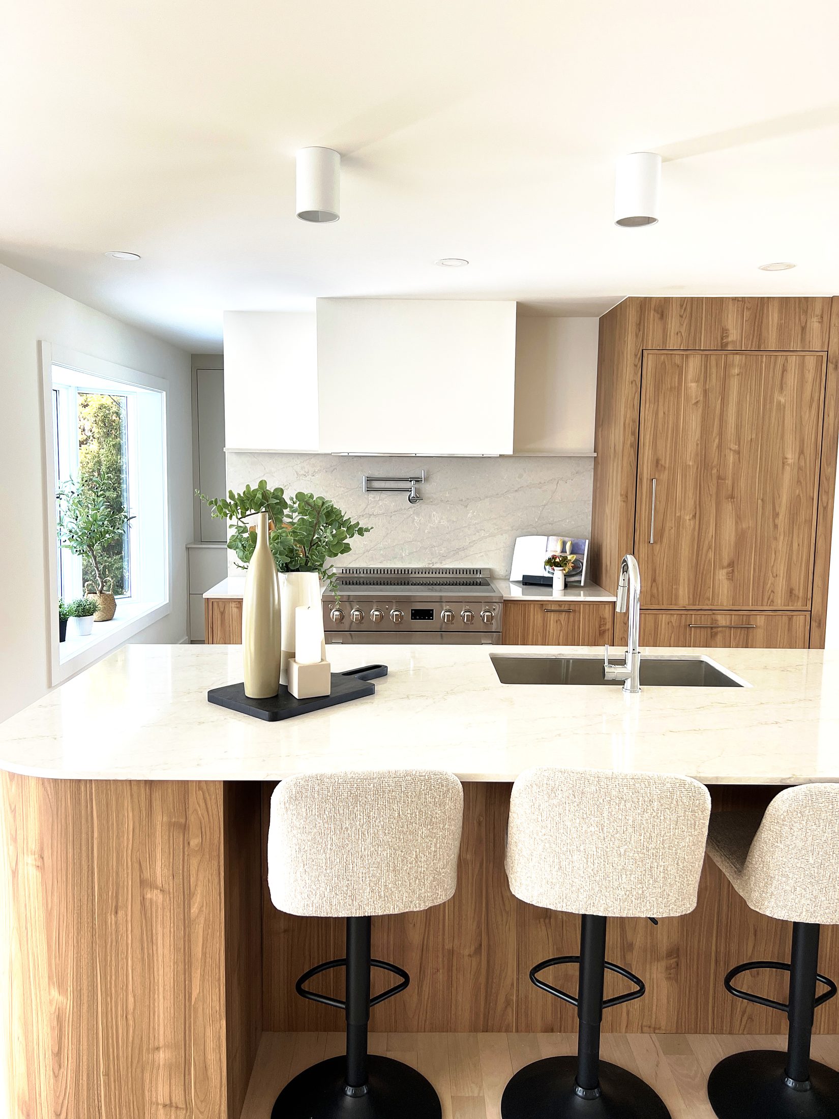 Cuisine lumineuse avec îlot arrondi en bois, comptoir de quartz et tabourets bouclés.